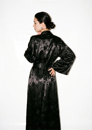 Back of the Tenebrae robe on model, three-quarter view with the belt tied at the waist and the floral jacquard running the full length