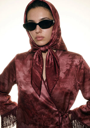 Close up of the Crimson Dusk silk scarf tied as a head scarf with a knot under the chin over the matching fringed crimson print set