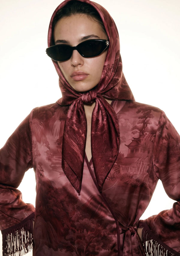 Close up of the Crimson Dusk silk scarf tied as a head scarf with a knot under the chin over the matching fringed crimson print set