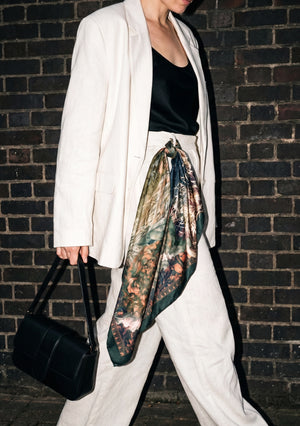 Eostra silk scarf knotted at the waist over a cream linen suit, the teal and copper hare print falling in a long point