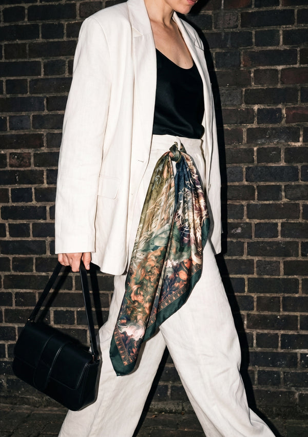 Eostra silk scarf knotted at the waist over a cream linen suit, the teal and copper hare print falling in a long point